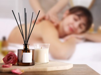 Image of Spa therapy. Woman receiving massage on table and composition with aromatic reed air freshener in salon, selective focus