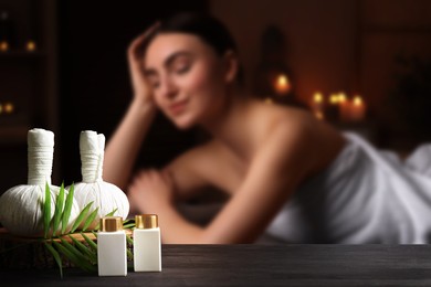 Image of Spa therapy. Woman lying on massage table and composition with body care products and herbal bags in salon, selective focus