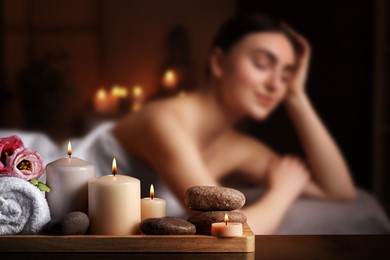 Image of Spa therapy. Woman lying on massage table and composition with candles, stones and towel in salon, selective focus