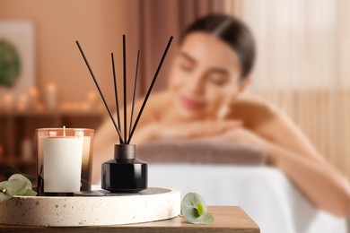 Image of Spa therapy. Woman lying on massage table and composition with aromatic reed air freshener in salon, selective focus