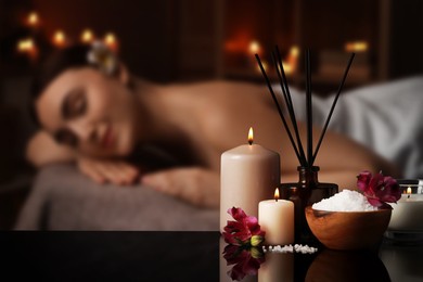 Image of Spa therapy. Woman lying on massage table and composition with reed air freshener and candles in salon, selective focus