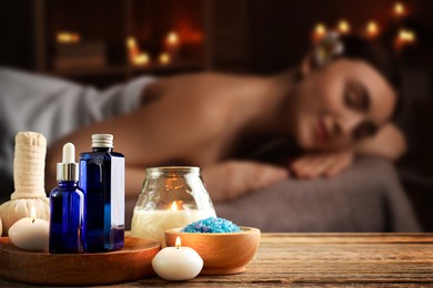 Image of Spa therapy. Woman lying on massage table and composition with body care products and candles in salon, selective focus