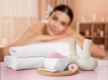 Image of Spa therapy. Woman lying on massage table and composition with sea salt, herbal bags and towels in salon, selective focus
