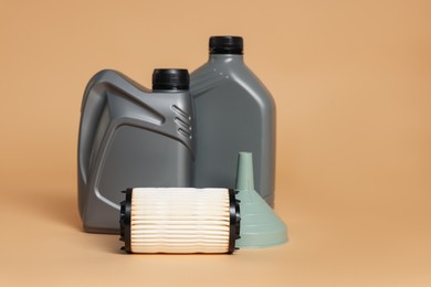 Photo of Motor oil in plastic canisters, filter and funnel on beige background, space for text
