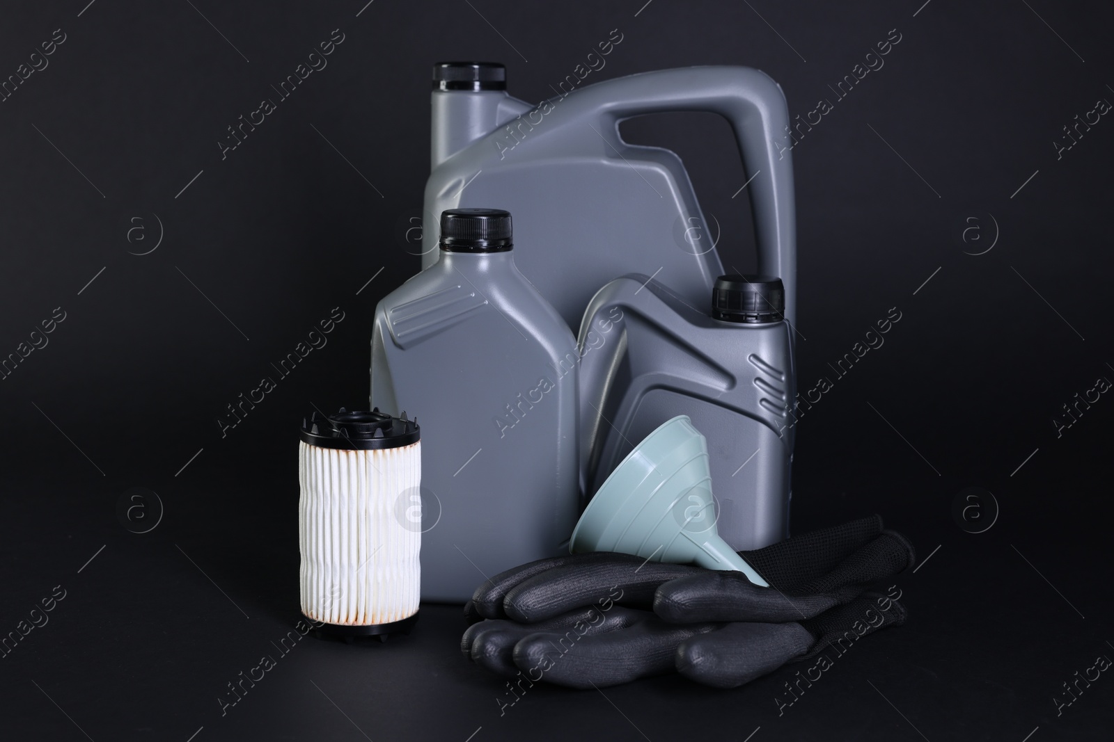 Motor oil in plastic canisters, filter, gloves and funnel on black background Photo of Motor oil in plastic canisters, filter, gloves and funnel on black background