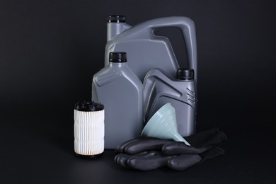 Photo of Motor oil in plastic canisters, filter, gloves and funnel on black background
