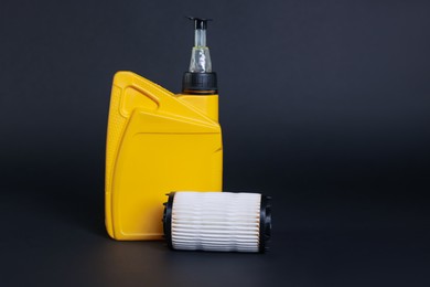Photo of Motor oil in plastic canister and filter on dark grey background, space for text