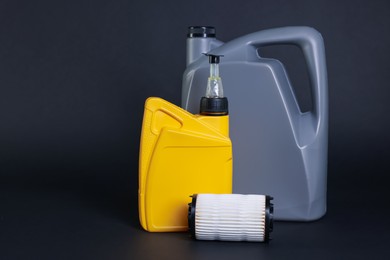 Photo of Motor oil in plastic canisters and filter on dark grey background, space for text