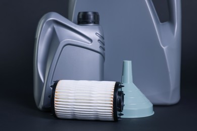 Photo of Motor oil in plastic canisters, filter and funnel on dark grey background, closeup