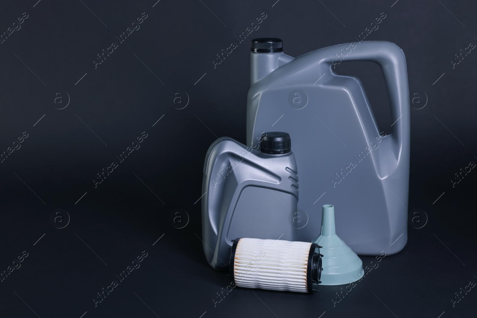 Motor oil in plastic canisters, filter and funnel on dark grey background, space for text Photo of Motor oil in plastic canisters, filter and funnel on dark grey background, space for text