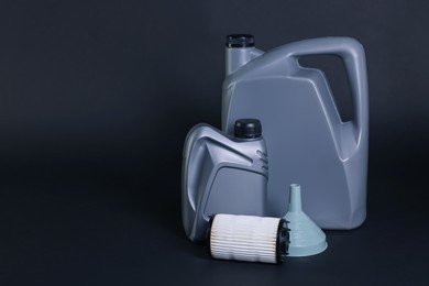 Photo of Motor oil in plastic canisters, filter and funnel on dark grey background, space for text