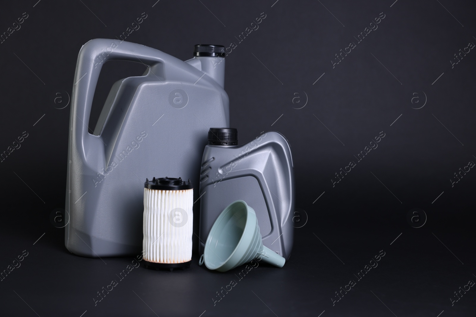 Motor oil in plastic canisters, filter and funnel on black background, space for text Photo of Motor oil in plastic canisters, filter and funnel on black background, space for text