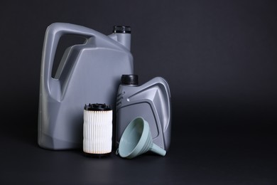 Photo of Motor oil in plastic canisters, filter and funnel on black background, space for text