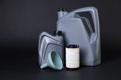 Photo of Motor oil in plastic canisters, filter and funnel on black background, space for text
