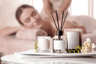 Image of Spa therapy. Woman receiving massage on table and composition reed air freshener and scented candles in salon, selective focus