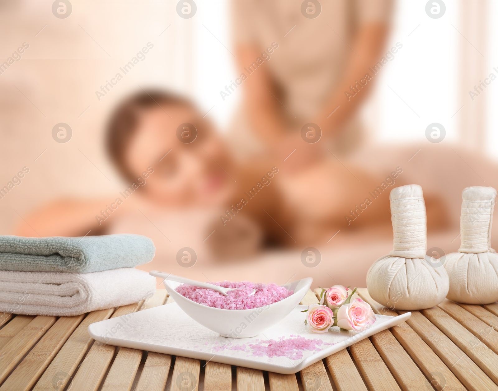 Spa therapy. Woman receiving massage on table and composition with sea salt, herbal bags and towels in salon, selective focus Image of Spa therapy. Woman receiving massage on table and composition with sea salt, herbal bags and towels in salon, selective focus