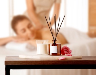 Image of Spa therapy. Woman receiving massage on table and composition with aromatic reed air freshener in salon, selective focus