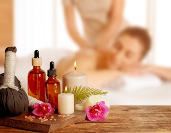Image of Spa therapy. Woman receiving massage on table and composition with herbal bags and body care products in salon, selective focus
