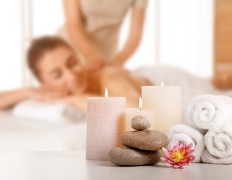 Image of Spa therapy. Woman receiving massage on table and composition with stones, candles and towels in salon, selective focus