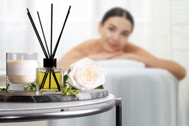 Image of Spa therapy. Woman lying on massage table and composition with reed air freshener in salon, selective focus