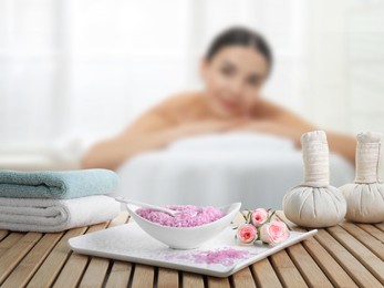 Image of Spa therapy. Woman lying on massage table and composition with sea salt, herbal bags and towels in salon, selective focus