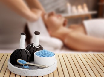 Image of Spa therapy. Woman receiving massage on table and composition with herbal bags and sea salt in salon, selective focus