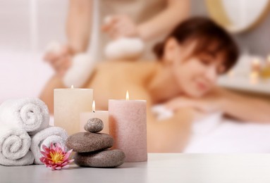 Image of Spa therapy. Woman receiving massage on table and composition with stones, candles and towels in salon, selective focus