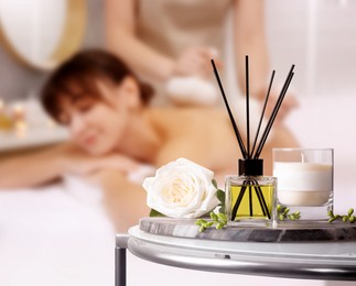Image of Spa therapy. Woman receiving massage on table and composition with aromatic reed air freshener in salon, selective focus