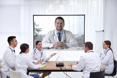 Image of Team of doctors using video projector during conference indoors. Speaker on projection screen
