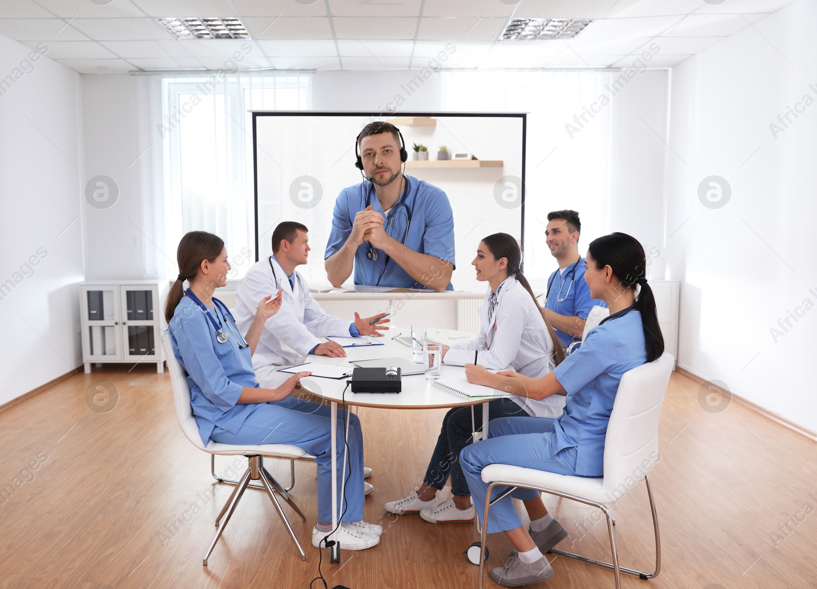 Team of doctors using video projector during conference indoors. Speaker on projection screen Image of Team of doctors using video projector during conference indoors. Speaker on projection screen