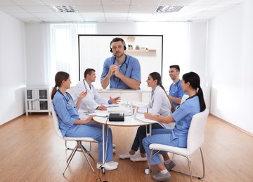Image of Team of doctors using video projector during conference indoors. Speaker on projection screen