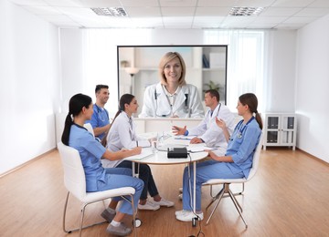Image of Team of doctors using video projector during conference indoors. Speaker on projection screen