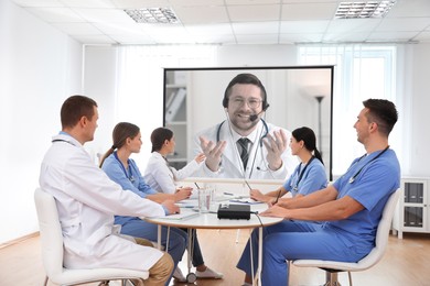 Image of Team of doctors using video projector during conference indoors. Speaker on projection screen