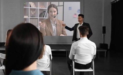 Image of Group of people participating in business conference indoors. Speaker on projection screen