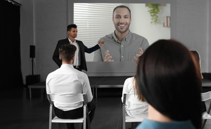 Image of Group of people participating in business conference indoors. Speaker on projection screen