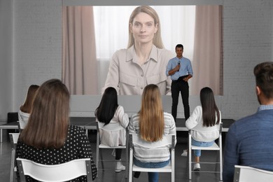 Image of Group of people participating in business conference indoors. Speaker on projection screen