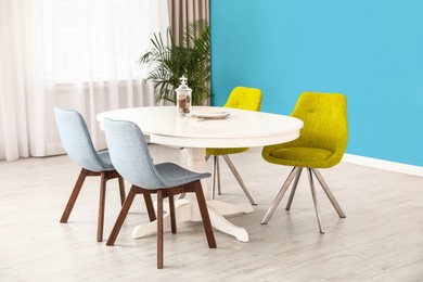 Image of Dining table and colorful chairs near light blue wall in room. Interior design