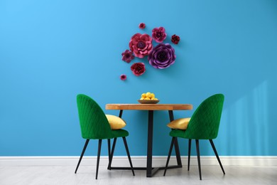 Image of Dining table and green chairs near light blue wall with floral decor in room. Interior design