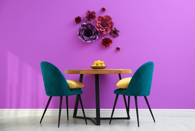 Image of Dining table and blue chairs near violet wall with floral decor in room. Interior design