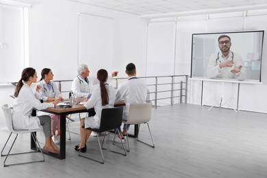 Image of Team of doctors using video projector during conference indoors. Speaker on projection screen