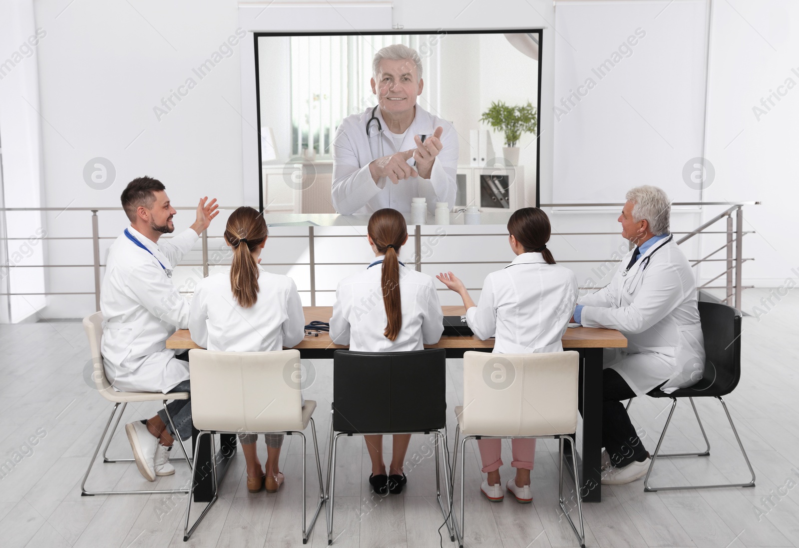 Team of doctors using video projector during conference indoors. Speaker on projection screen Image of Team of doctors using video projector during conference indoors. Speaker on projection screen