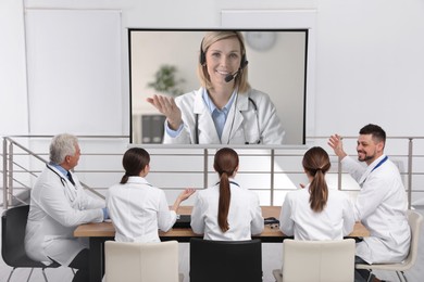 Image of Team of doctors using video projector during conference indoors. Speaker on projection screen