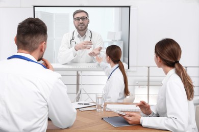 Image of Team of doctors using video projector during conference indoors. Speaker on projection screen