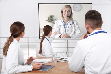 Image of Team of doctors using video projector during conference indoors. Speaker on projection screen