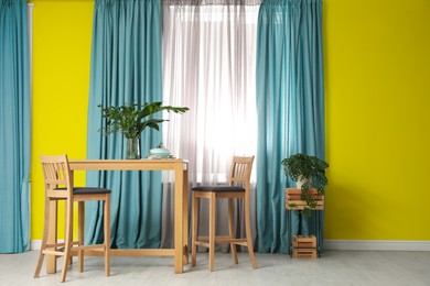 Image of Dining table and chairs near window and yellow wall in room. Interior design