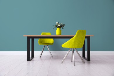 Image of Dining table and yellow chairs near teal color wall in room. Interior design