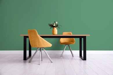 Image of Dining table and orange chairs near green wall in room. Interior design