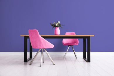 Image of Dining table and pink chairs near indigo color wall in room. Interior design