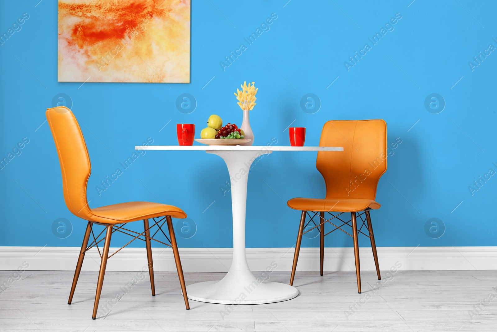 Dining table and orange chairs near light blue wall in room. Interior design Image of Dining table and orange chairs near light blue wall in room. Interior design