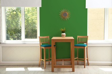 Image of Dining table and chairs near green wall and windows in room. Interior design